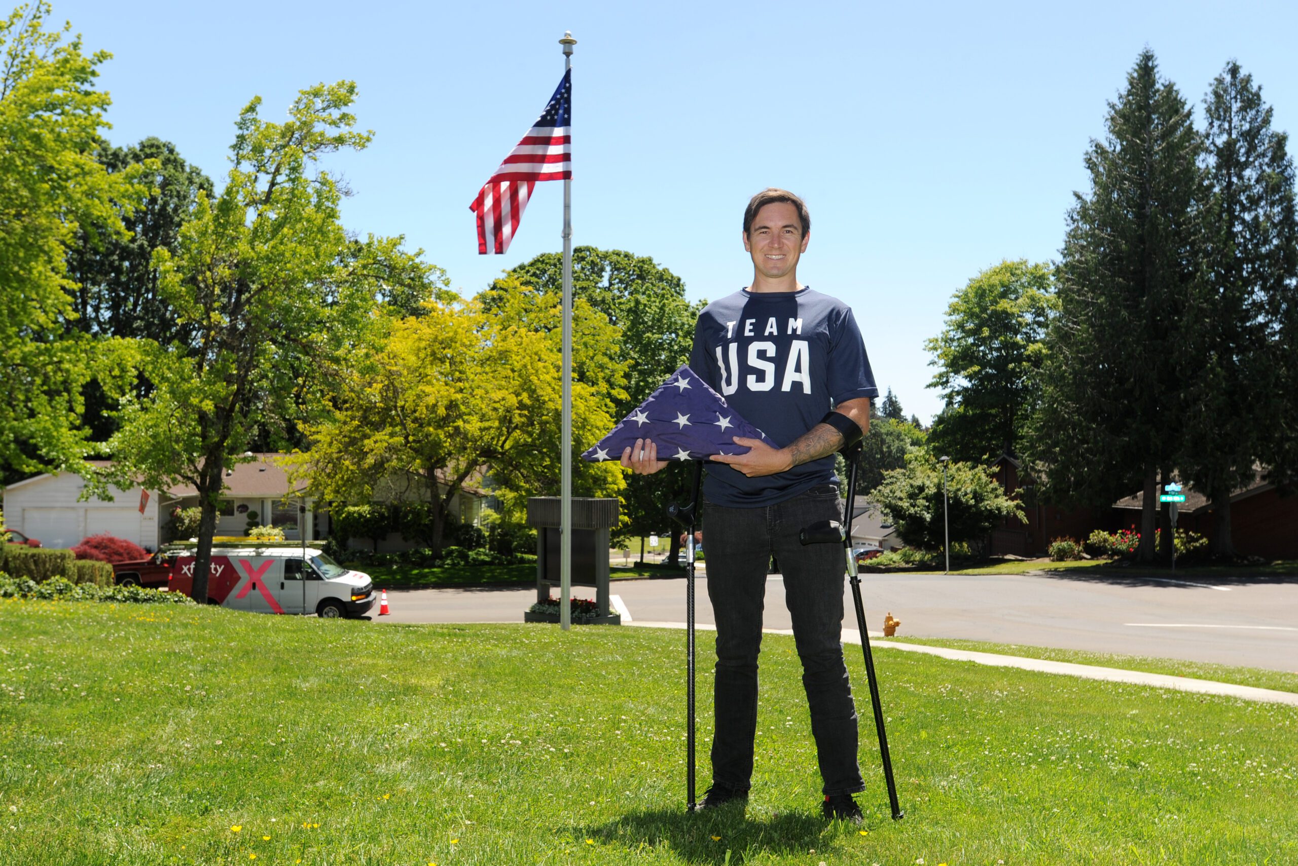 A man stands in front of a flag pole with an Americna flag on in a park.